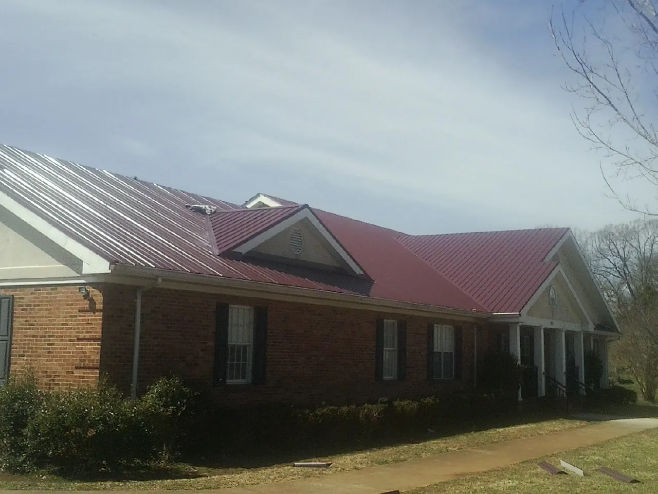 Red metal roof with gabled entries on a long brick building, from a Hail Damage Roof Repair job in Waymart