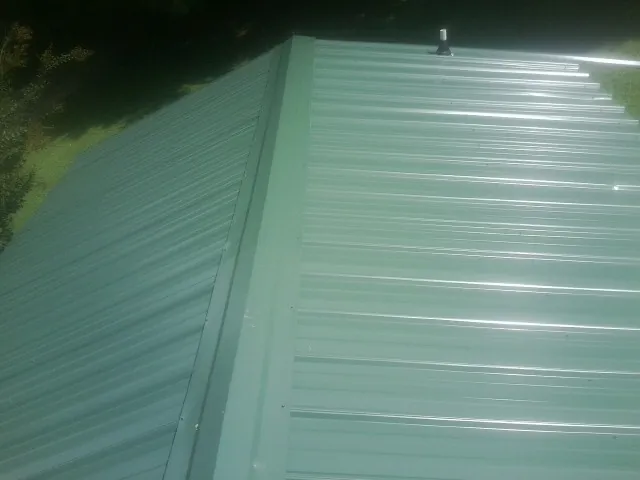 New green metal panels meeting at the ridge of a roof — Flat Roof Repair work by our crew in Waymart