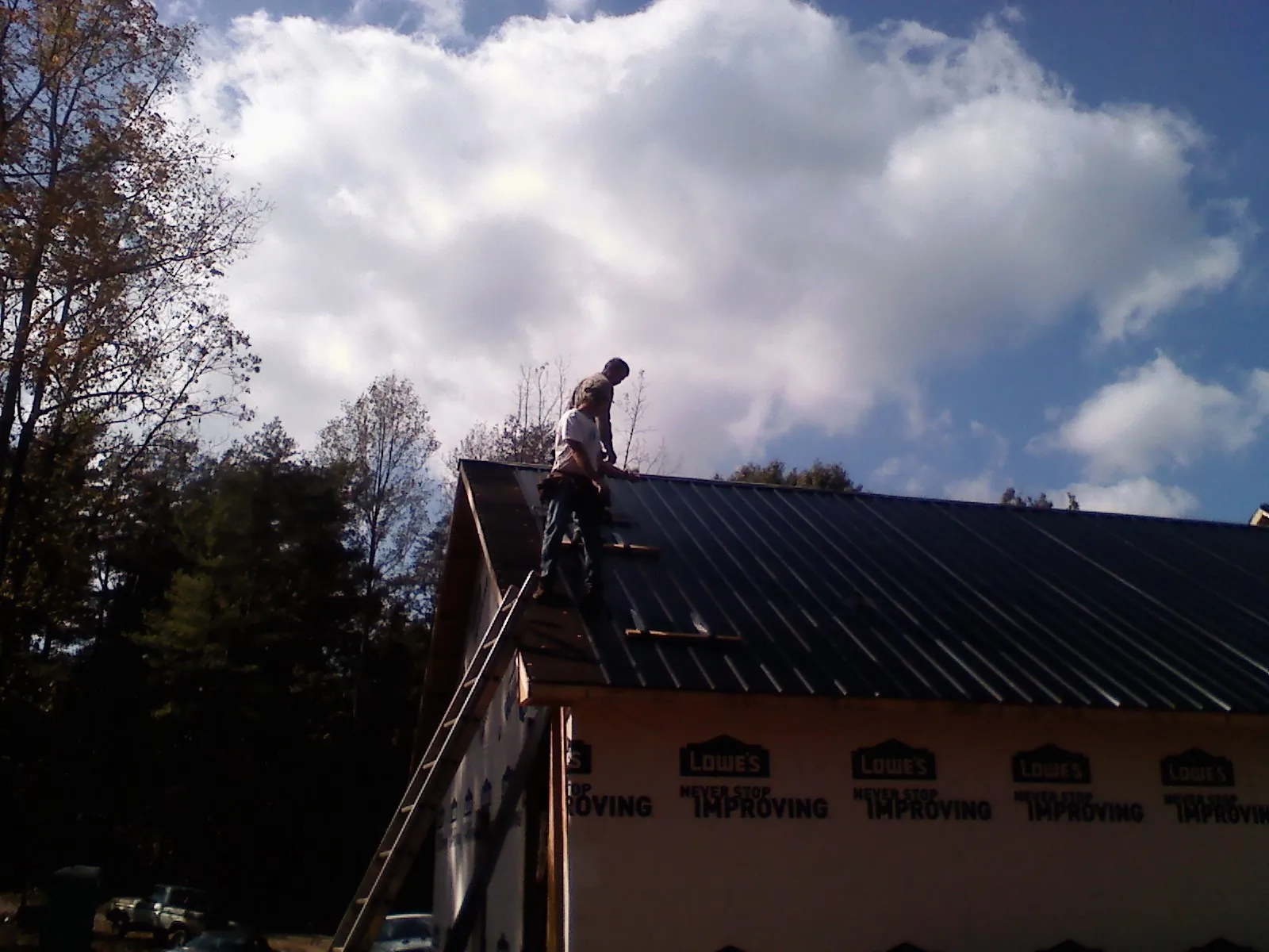Roofer fastening dark metal panels high against a cloudy sky, from a Roof Inspection job in Waymart