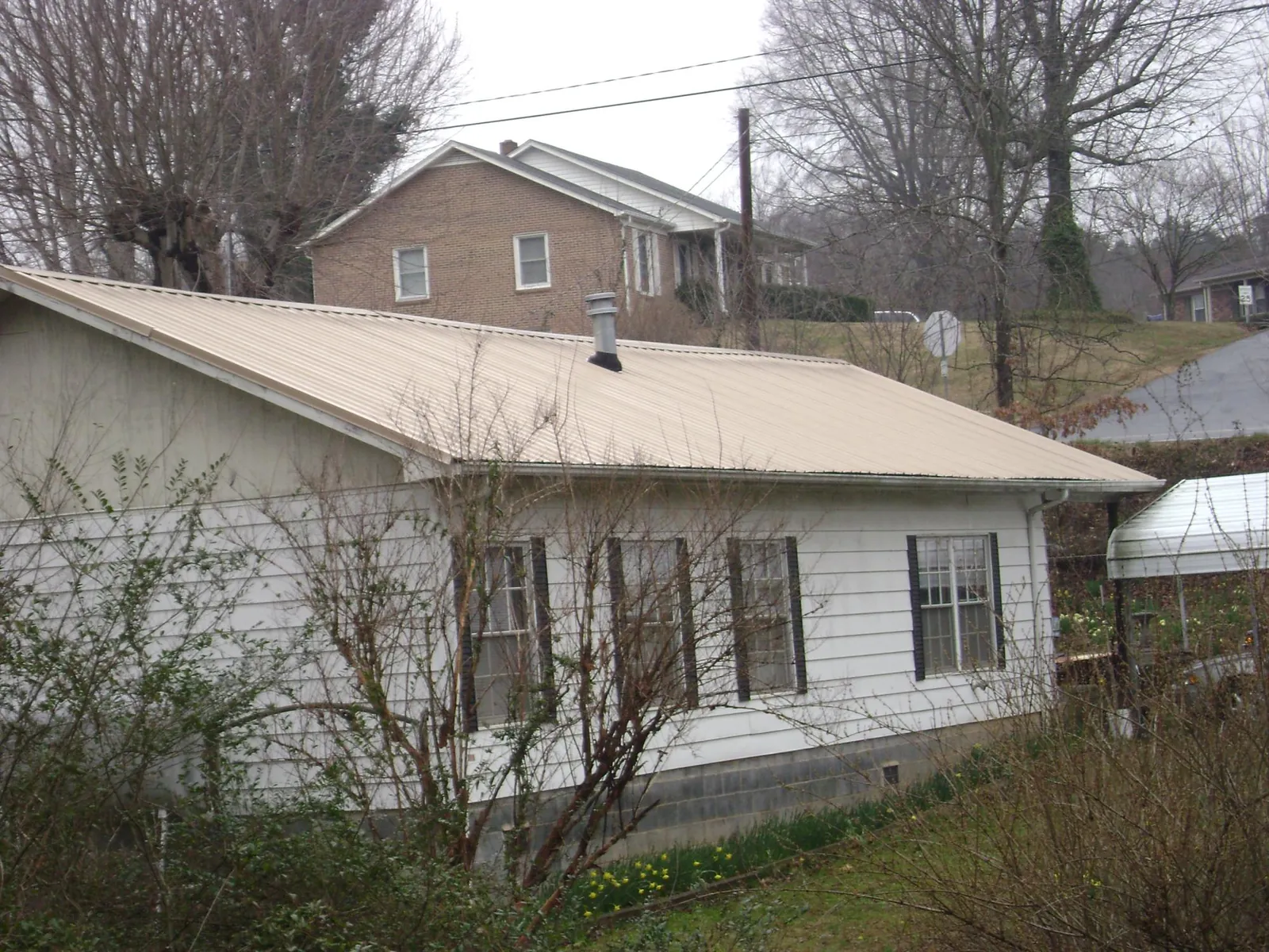 Tan metal roof on a white sided house set into a hillside — Commercial Roofing by Roofing Brothers in Waymart